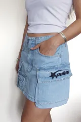 Minifalda color beige con bolsillos tipo cargo y bordado rojo con forma de estrella y texto en el bolsillo lateral.