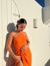 Vestido largo naranja de crepé con escote halter y falda tipo pareo con abertura lateral.