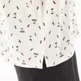 Remera polo blanca de piqué de algodón con estampado de palmeras y tablas de surf.
