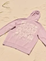 Buzo con capucha color lila, de algodón y fit relajado. Presenta un estampado con una palmera y el texto "Rainbow Bay" en el pecho.