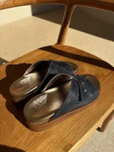 Sandalias de cuero color azul marino con plantilla dorada y suela marrón. Presentan una tira ancha cruzada con doble remache dorado.