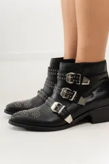 Botas cortas de cuero negro con puntera fina, taco bajo y cierre lateral. Presentan tres correas con hebillas plateadas y apliques de tachas plateadas.
