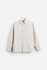 Camisa color crema de corte relaxed fit, confeccionada en tejido de mezcla de algodón suave al tacto. Tiene cuello solapa, manga larga con puños abotonados, un bolsillo de parche en el pecho y cierre frontal con botones.