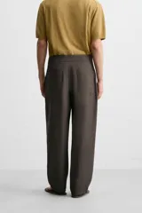 Pantalón marrón oscuro de corte amplio, con cintura ajustable con cordón, bolsillos plastrón delanteros y traseros, detalle de costuras frontales y cierre frontal con cremallera y gancho metálico oculto.