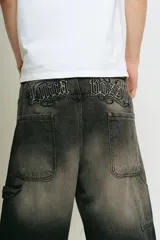 Bermuda de jean negro lavado, corte baggy carpintero, con bordado gótico en la parte trasera, bolsillos grandes, bolsillo lateral y tira carpintera lateral.