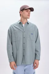 Sobrecamisa verde con rayas verticales blancas, de corte holgado, manga larga, cuello camisero y dos bolsillos frontales con solapa.