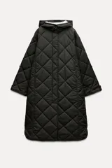 Chaqueta larga acolchada color negro con capucha y manga larga. Tiene bolsillos delanteros y bajo asimétrico con aberturas laterales. El cierre frontal es con botones ocultos por solapa.