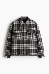 Sobrecamisa de franela de algodón a cuadros blancos, negros y grises. Corte oversized, cuello inglés, tapeta con botones a presión, canesú en la espalda, bolsillos superiores con solapa y botón a presión, bolsillos laterales y bajo recto con aberturas laterales. Mangas largas con tapeta y botón a presión en los puños. Forro guateado.