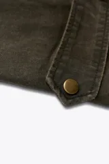Trench color verde oscuro con cuello solapa combinado en pana marrón y manga larga. Detalle de acabados con trabillas y pinza en espalda. Bolsillos delanteros con solapa y botón a presión. Tejido encerado efecto lavado. Cierre frontal con botones a presión.