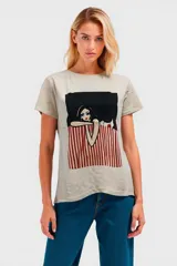 Remera color beige con estampado de una ilustración de una mujer con cabello negro y un vestido a rayas rojas y blancas.