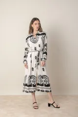 Vestido camisero midi de lino y viscosa color crudo con estampado de palmeras en negro. Tiene cuello camisero, mangas largas con puños y cinturón de la misma tela.