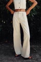 Pantalón de jean color crudo, de tiro alto y corte bootcut. Presenta cinturón fino del mismo tejido, bolsillos de parche en la parte trasera y cierre frontal con cremallera y botón.