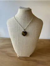 Collar con cadena plateada y dije de piedra natural ojo de tigre tallada en forma de corazón.