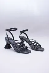 Sandalias negras con tiras lisas y trenzadas en el empeine, y una tira trenzada que se ajusta al tobillo con hebilla. Tienen un tacón geométrico.