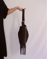 Bolso tipo bandolera de cuero negro con flecos y tachas plateadas. Tiene correa regulable, forro interior y bolsillo interno.