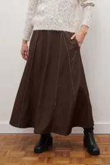 Falda larga de jean azul oscuro, corte acampanado con paneles y costuras visibles.