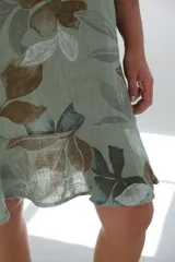 Vestido corto verde con estampado de hojas marrones y blancas, sin mangas y con volado en el ruedo.