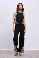 Pantalón negro de corte ancho y tiro alto, con bordados estilo paisley en color crudo o beige claro en el ruedo y en el contorno del top a juego.