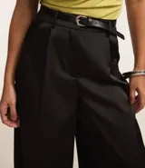 Pantalón pantalona de corte sastre, color negro, con trabillas en la cintura, cinturón con hebilla de metal y pliegues delanteros.