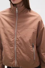 Campera de corte holgado en color tostado, confeccionada en poliamida. Presenta cuello alto, cierre frontal con cremallera, bolsillos laterales con cierre y cordón ajustable en el ruedo.