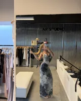 Vestido largo ajustado, sin mangas, con escote drapeado tipo halter y textura plisada. Presenta un estampado tie-dye en tonos blanco y negro/azul oscuro.