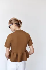 Chaqueta color marrón de tejido de punto, con cuello solapa, manga corta y bajo evasé con volantes. Cierre frontal con botones forrados a tono.