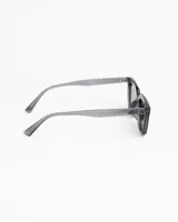 Lentes de sol de montura cuadrada gruesa, color gris ahumado translúcido, con cristales oscuros polarizados. Presentan detalles metálicos en las esquinas superiores del frente.