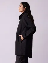 Gabardina negra impermeable con capucha desmontable, cierre central con cremallera y botones a presión, bolsillos delanteros y forro interno.