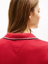Vestido rojo de corte slim, tipo chomba, con cuello polo y tapeta de botones. Tiene mangas cortas con ribete blanco y logo de Tommy Hilfiger bordado en el pecho.