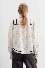 Camisa cruda de algodón con calce relajado y cuello redondo. Detalles de velvet negro y broderie en escote, puños y ruedo.