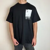 Remera negra de corte oversize con estampado rectangular de palmeras en el pecho.