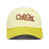 Gorro estilo dad hat de dos tonos de amarillo. La corona es de color amarillo pálido y la visera es de un amarillo más intenso. Bordado frontal con el texto "Critical" en color borgoña y la palabra "Slide" debajo en un patrón de puntos.