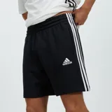 Short deportivo negro de algodón French Terry, con cintura elástica y cordón ajustable. Presenta las tres franjas blancas características de Adidas en los laterales y el logo de Adidas bordado en blanco en la pierna izquierda.