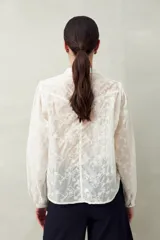 Camisa blanca con bordado floral en contraste, cuello mao, abotonadura frontal y mangas largas con frunces en los hombros.