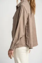 Camisa color marrón claro de gamuza vegana con calce oversize, cuello clásico, cierre frontal con botones y mangas largas con puños abotonados.