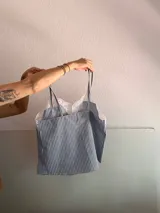 Top celeste y blanco a rayas verticales con breteles finos y detalle de encaje en el escote.