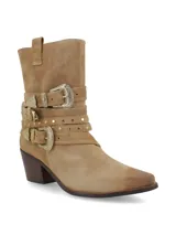 Bota corta de cuero gamuza color beige, con taco de madera y punta fina. Presenta tres tiras con hebillas metálicas plateadas y tachas pequeñas alrededor del tobillo.
