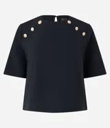 Blusa negra de crepé con cuello redondo, mangas cortas y botones decorativos dorados en los hombros.