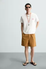 Camiseta blanca de corte recto, cuello redondo y manga corta. Estampado pequeño en el frente y estampado grande en la espalda con texto en color rojo.