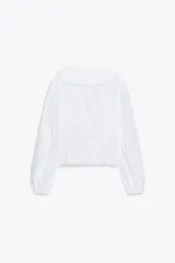 Camisa blanca de popelina de algodón con cuello bobo y mangas largas con elástico en los puños. Detalle de puntilla a tono en cuello y ruedo. Cierre frontal con botones.