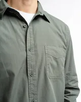 Camisa de manga larga color verde oliva, confeccionada en algodón. Tiene corte clásico, bolsillo en el lado izquierdo del pecho y cierre con botones.