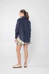 Camisa azul marino de lino con cuello clásico, cierre frontal con botones color madera, mangas largas con puños con detalle de ribete marrón y bordado de ave en el cuello.