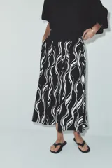 Falda midi de tiro alto con estampado de líneas onduladas blancas sobre fondo negro. Presenta bolsillos ocultos en la costura, detalle de tablas en el delantero y cierre lateral con cremallera oculta.