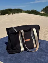 Bolso tipo tote bag negro con asas doradas y cierre superior.