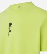 Remera color amarillo flúor de corte recto, con cuello redondo y manga corta. Presenta un bordado de una rosa negra en el lado izquierdo del pecho.