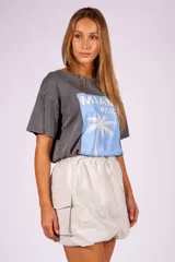 Falda corta negra de material ligero y brillante, con cintura elástica fruncida y bolsillos cargo frontales. El ruedo tiene un efecto abullonado o globo.