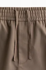 Pantalón de vestir color beige, de corte slim fit, con cintura elástica y cordón ajustable.