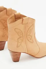 Botín de cuero color beige, estilo cowboy, con bordados en forma de mariposa en los laterales y taco de madera.
