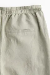 Pantalón de lino color verde claro, de tiro alto con cintura elástica, bolsillos al bies y bolsillos atrás insertados. Piernas rectas con pliegue cosido adelante.