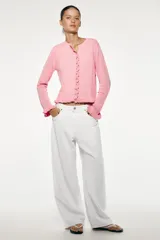 Chaqueta de punto rosa con cuello redondo y manga larga. Detalle de volantes en los bordes y cierre frontal con botones.